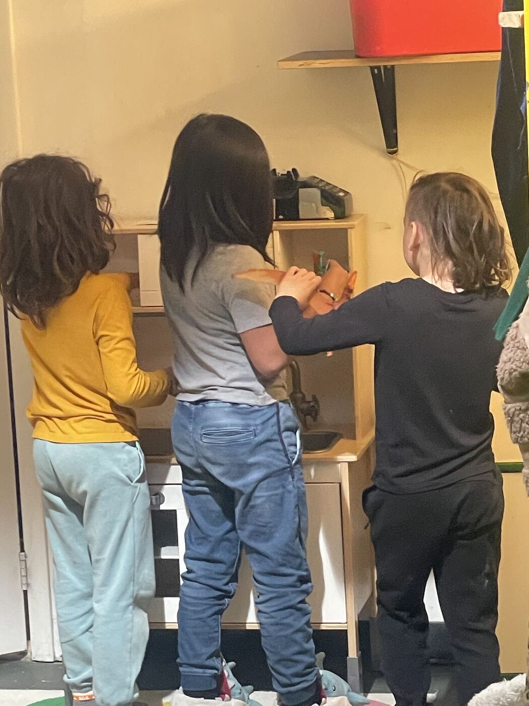 Three children from behind at a play kitchen