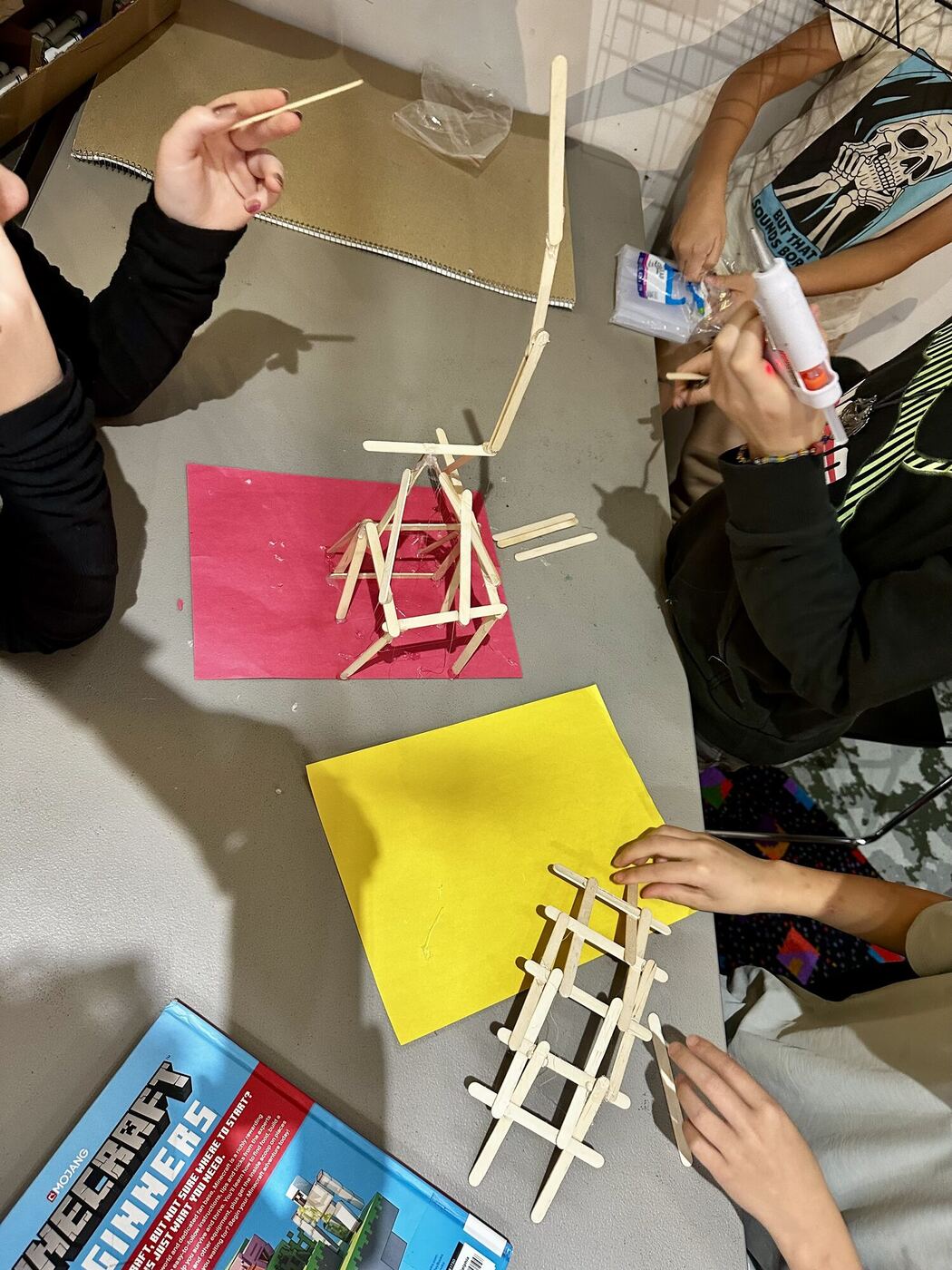 Hands gluing popsicle-stick towers on colored card