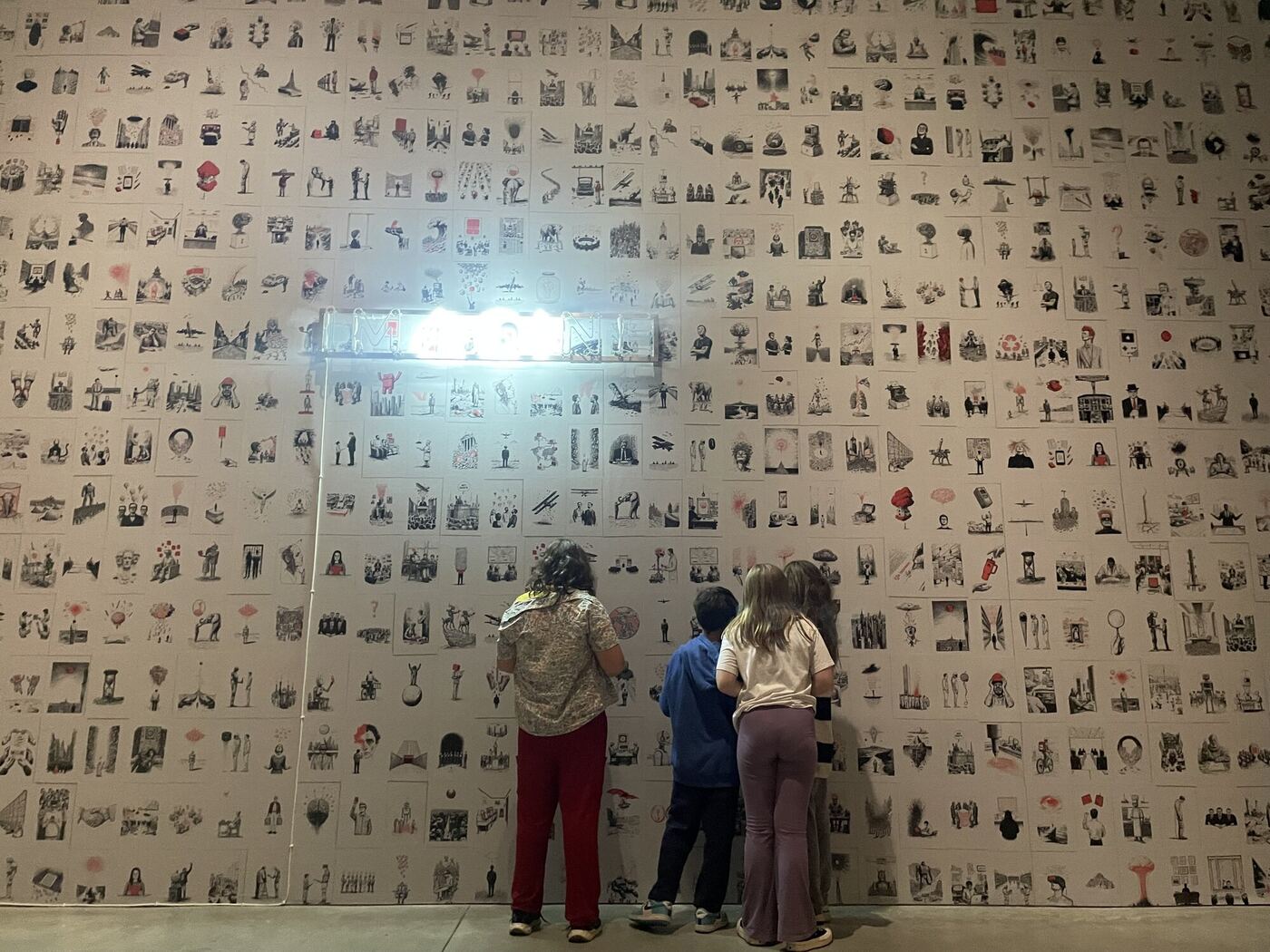 A wall of hundreds of small drawings at the art museum, three visitors seen from behind