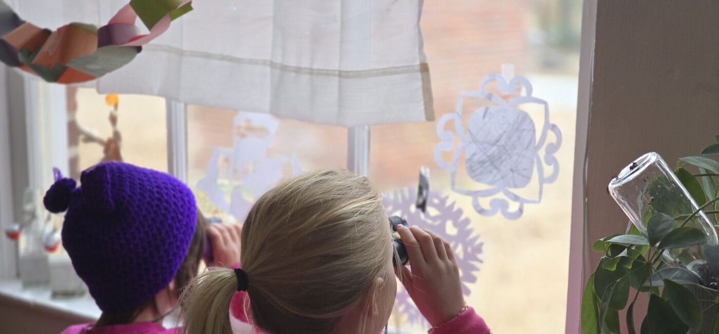 Two learners from behind at a classroom window, looking out through binoculars